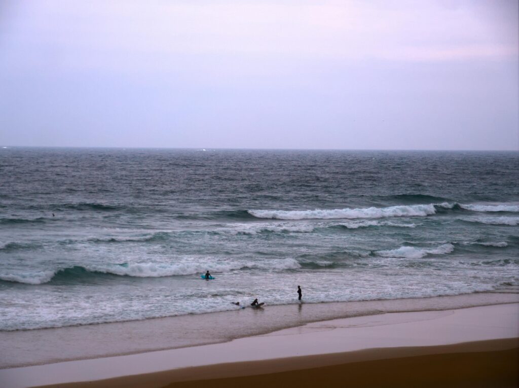 A tranquil beach at dusk with gentle waves and few people enjoying the calm atmosphere.