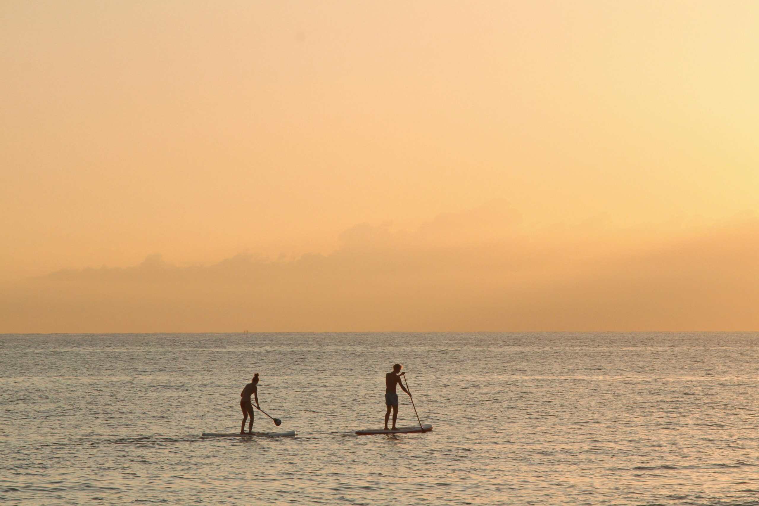 Two people paddleboarding at sunset in the tranquil waters of Barcelona.